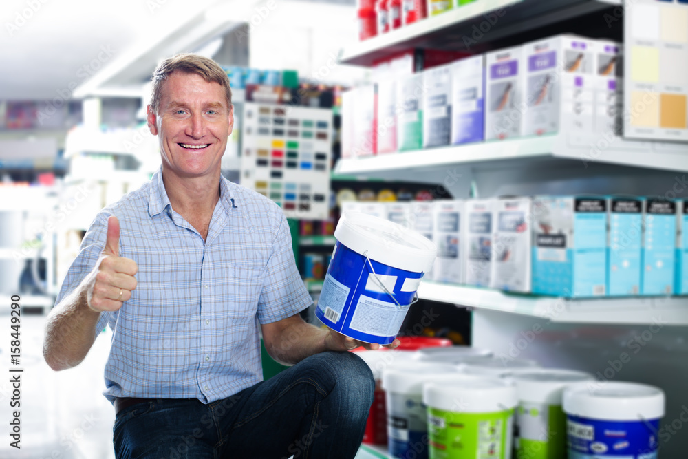 smiling man customer choosing paint bucket in hypermarket