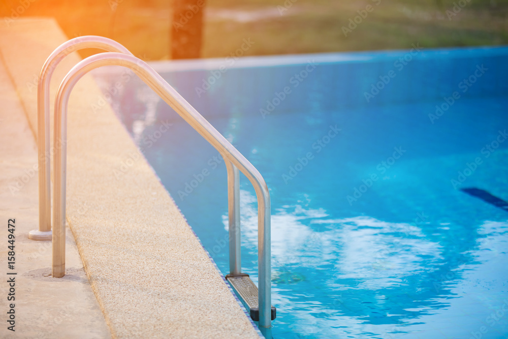 Grab bars ladder in the blue swimming pool with Orange sun light in mornung Grab bars ladder in the blue swimming pool with Orange sun light in mornung