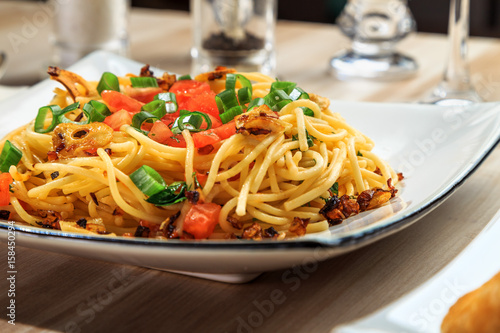 spaghetti with tomatoes, roasted garlic and green onions on a beautiful rectangular plate are on the table