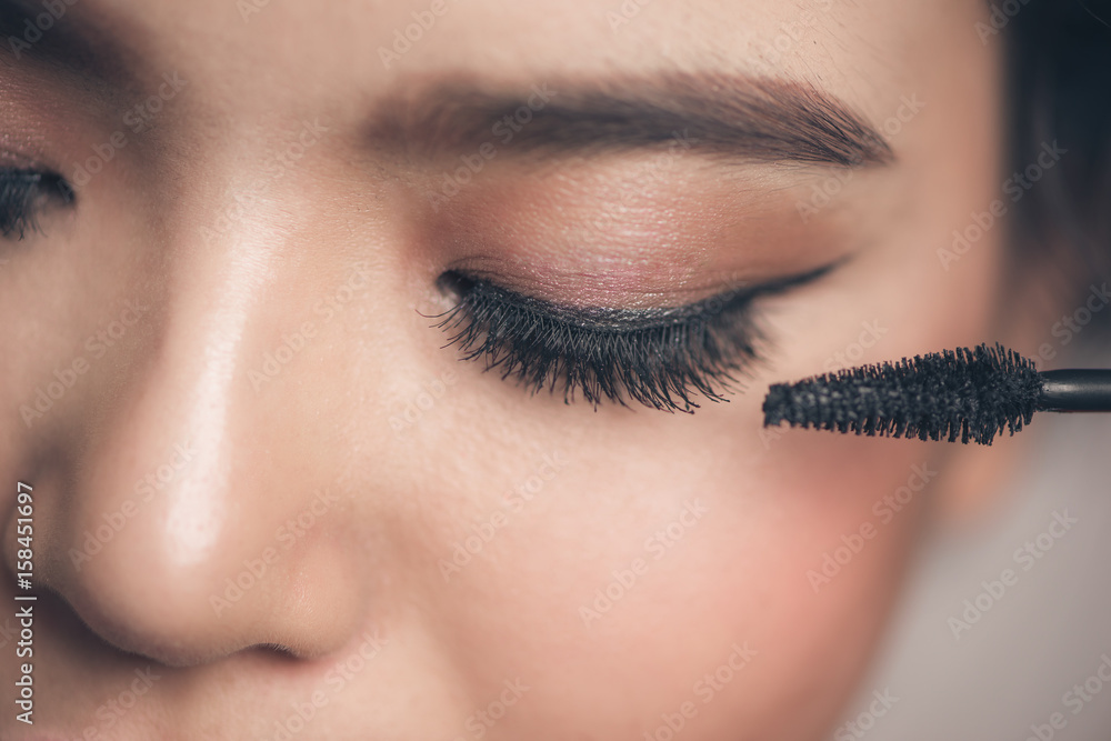 Close-up portrait of beautiful girl touching black mascara to her lashes
