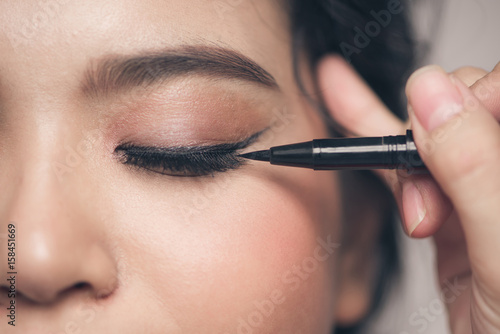 Close-up portrait of beautiful girl touching black eyeliner to her eyelid with closed eyes.