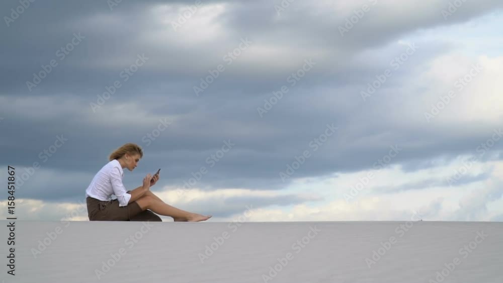 The blonde sits on top of a dune in the desert and prints on the phone The blonde sits on top of a dune in the desert and prints on the phone