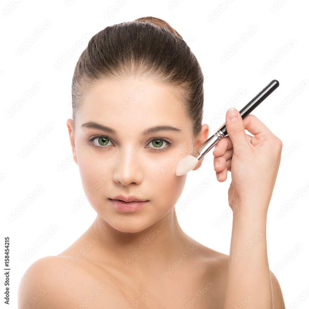 Portrait of beautiful young brunette woman with clean face. Beauty spa model girl with perfect fresh clean skin applying cosmetic brush. Youth and skin care concept. Isolated on a white background.