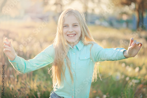Beautiful smiling teenage girl in blouse, against green of summer park. Sunlight, happiness, fun, hair, joy.