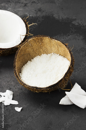 Half of ripe coconut and coconut shavings on a dark background
