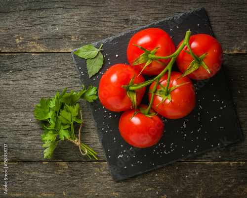 Branch with five ripe red tomatoes. Drops of water on ripe fruits. Green leaves and trunk.