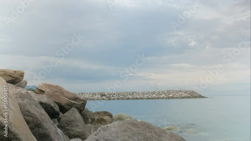 Stone pier on the sea. People walk along it swiftly, clouds float. TimeLapse photo