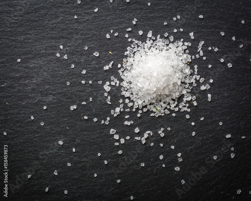 A bunch of white salt crystals on a black stone background. Seasoning for eating. Scattered over the surface.