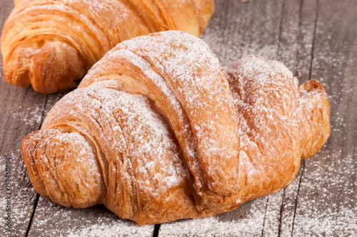 croissant sprinkled with powdered sugar on old wooden board