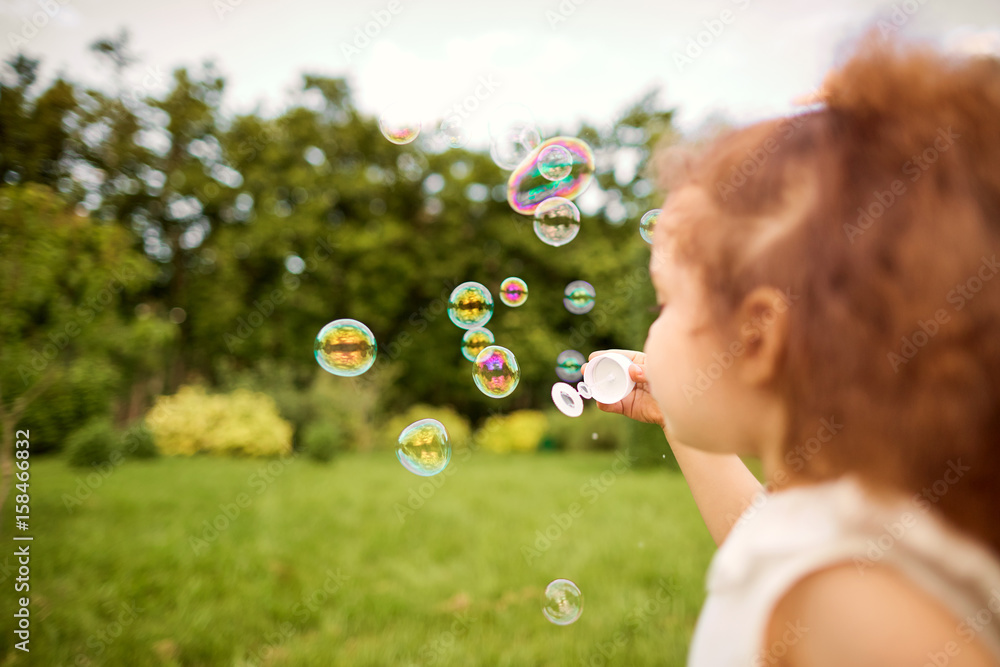 Child is playing with soap bubbles in the park. Background with soap bubbles.
