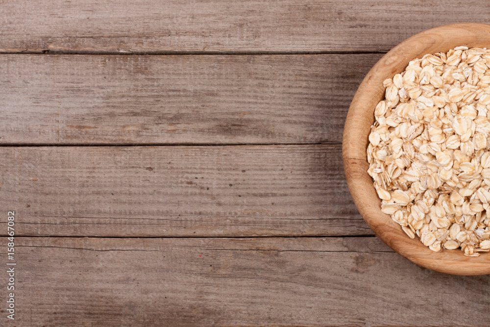 Oat flakes in a wooden bowl on old wooden background with copy space for your text. Top view Oat flakes in a wooden bowl on old wooden background with copy space for your text. Top view