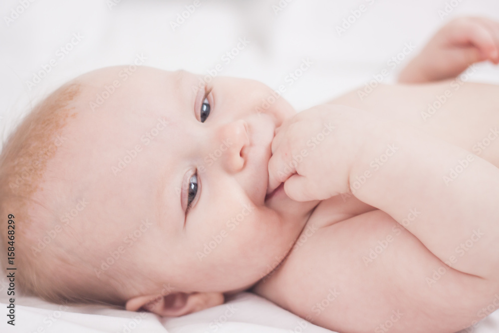 portrait of Cute baby with fingers in mouth in white bed portrait of Cute baby with fingers in mouth in white bed