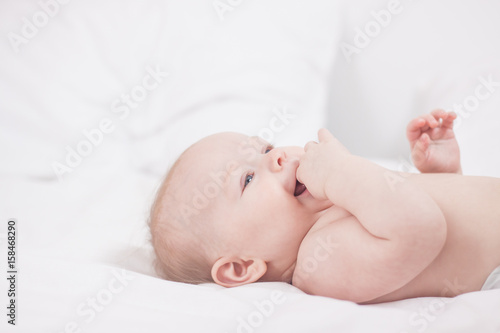 portrait of Cute baby with fingers in mouth in white bed