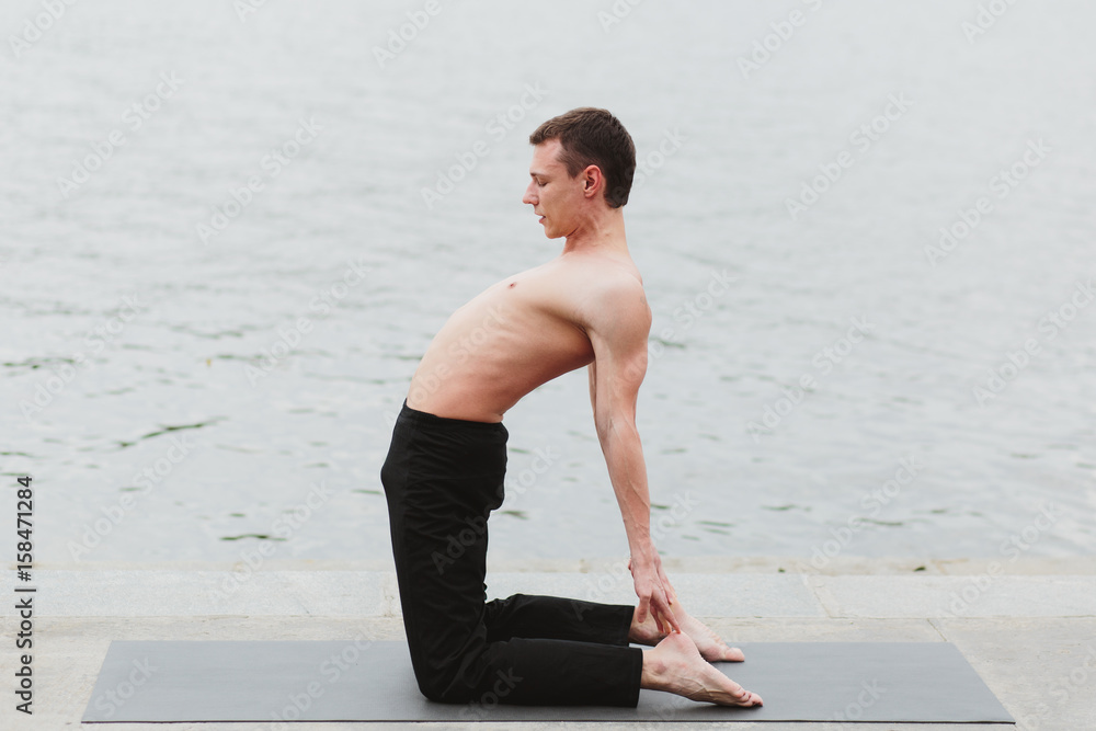 a young man practicing yoga asanas in the city on the waterfront