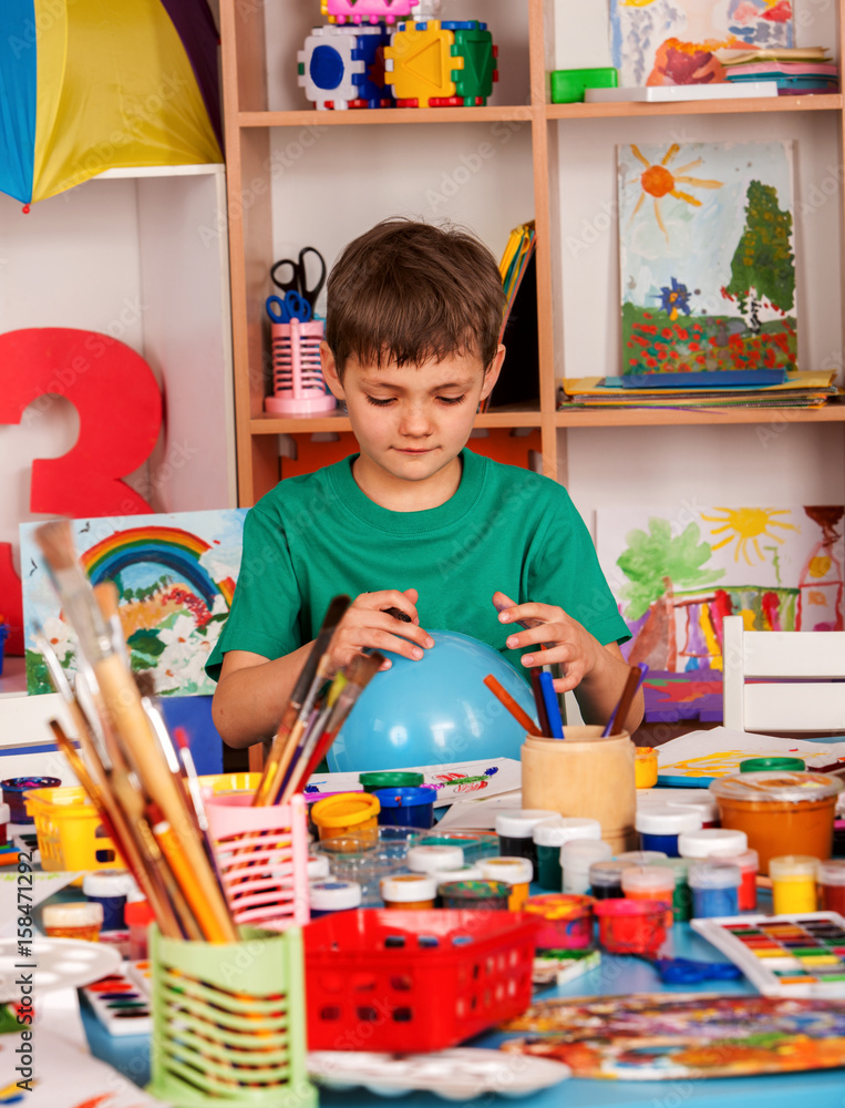 Fototapeta premium Small student boy painting in art school class. Child drawing by paints on table. Boy in a children's club. Craft drawing education develops creative abilities of children. Boy makes an imaginary