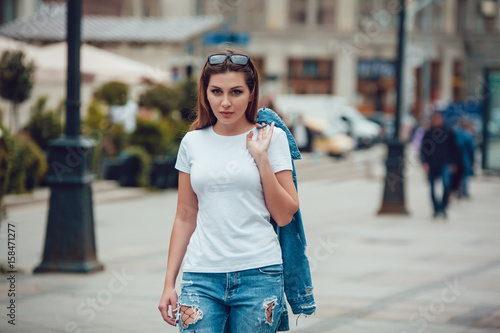 Attractive girl in a white T-shirt and jeans walking along the street. Mock-up.