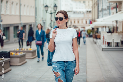 Attractive girl in sunglasses walking along the street. White t-shirt. Mock-up.