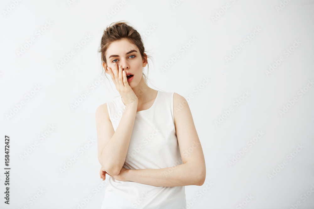 Bored tired young pretty girl hiding face behind hand looking at camera over white background. Bored tired young pretty girl hiding face behind hand looking at camera over white background.