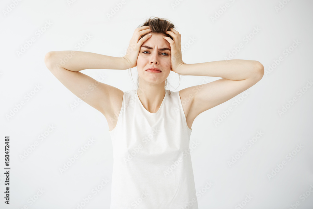 Displeased nervous young girl holding head looking at camera over white background. Displeased nervous young girl holding head looking at camera over white background.