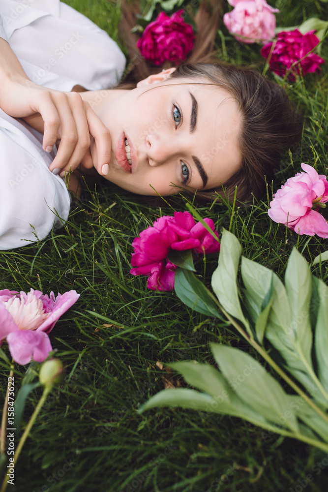 Woman lying on grass with flowers peonies around Woman lying on grass with flowers peonies around