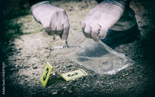 Crime scene investigation, picking up the tossed syringe and putting it to the plastic bag photo