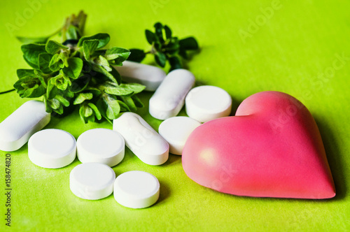 Herbs  pills and wooden heart on green background.