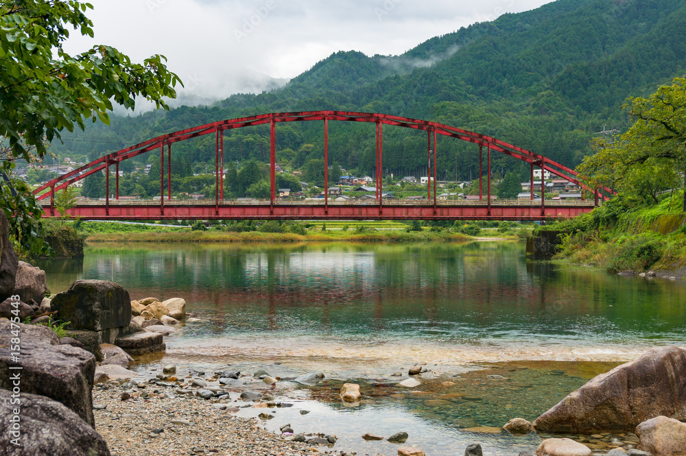 Japanese countryside landscape with bright red bridge over Kiso river