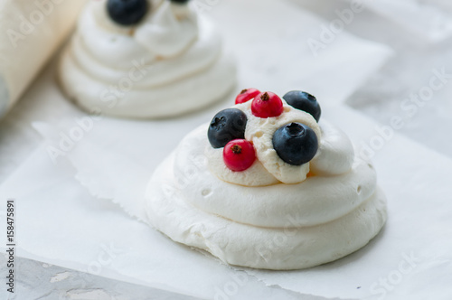 Close up of homemade individual meringue cakes Pavlova with mascarpone whipped cream garnished with fresh blueberries and red currants on a white stone background. Copy space.