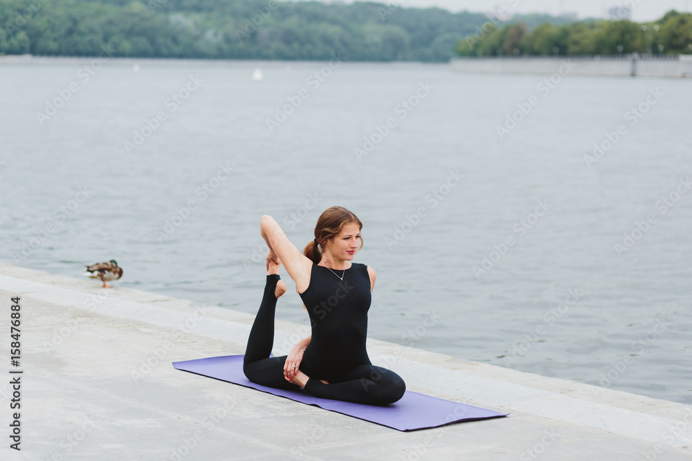 Fototapeta premium a young woman practicing yoga asanas in the city on the waterfront
