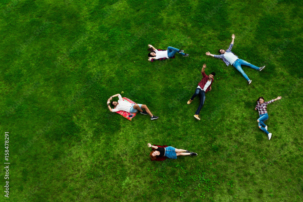 Group of young people laying on the grass in circle, happy, smiling