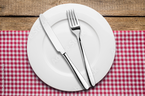 empty plate on a wooden background, a napkin in a red and white cage, a fork a knife