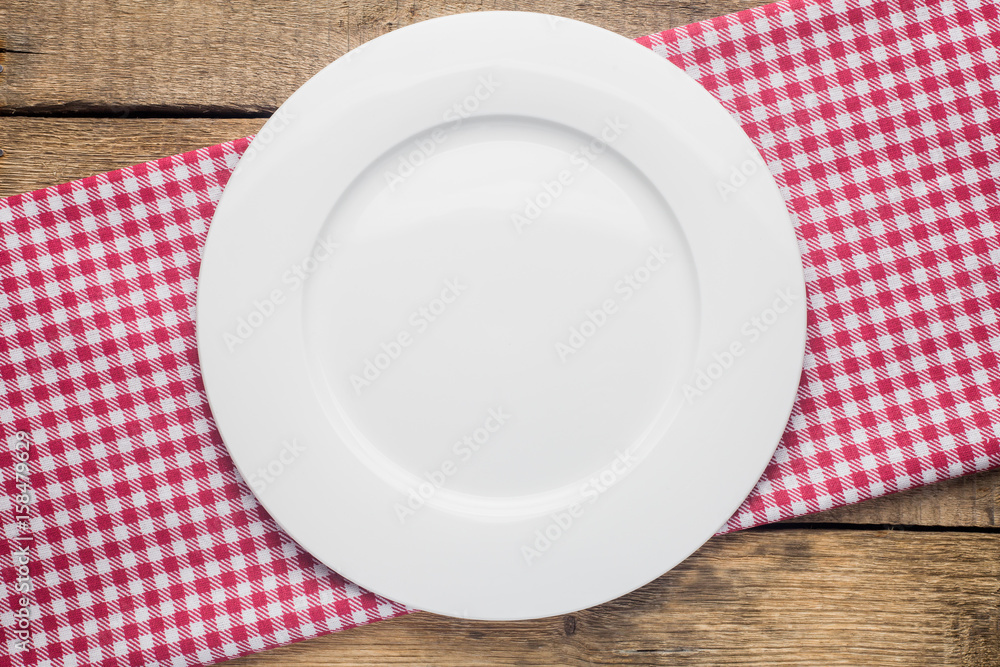 empty plate on a wooden background, a napkin in a red and white cage empty plate on a wooden background, a napkin in a red and white cage