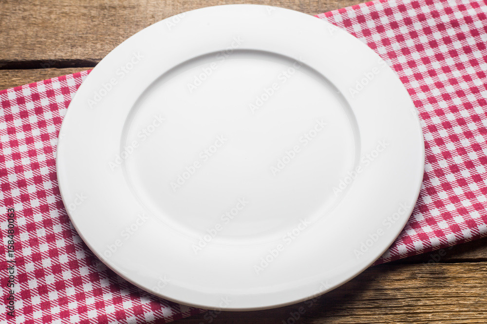empty plate on a wooden background, a napkin in a red and white cage empty plate on a wooden background, a napkin in a red and white cage