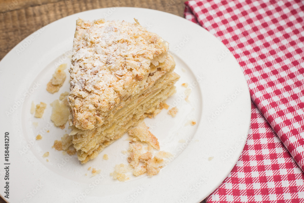 cake Napoleon on a white plate, on a wooden background and a red-white napkin cake Napoleon on a white plate, on a wooden background and a red-white napkin