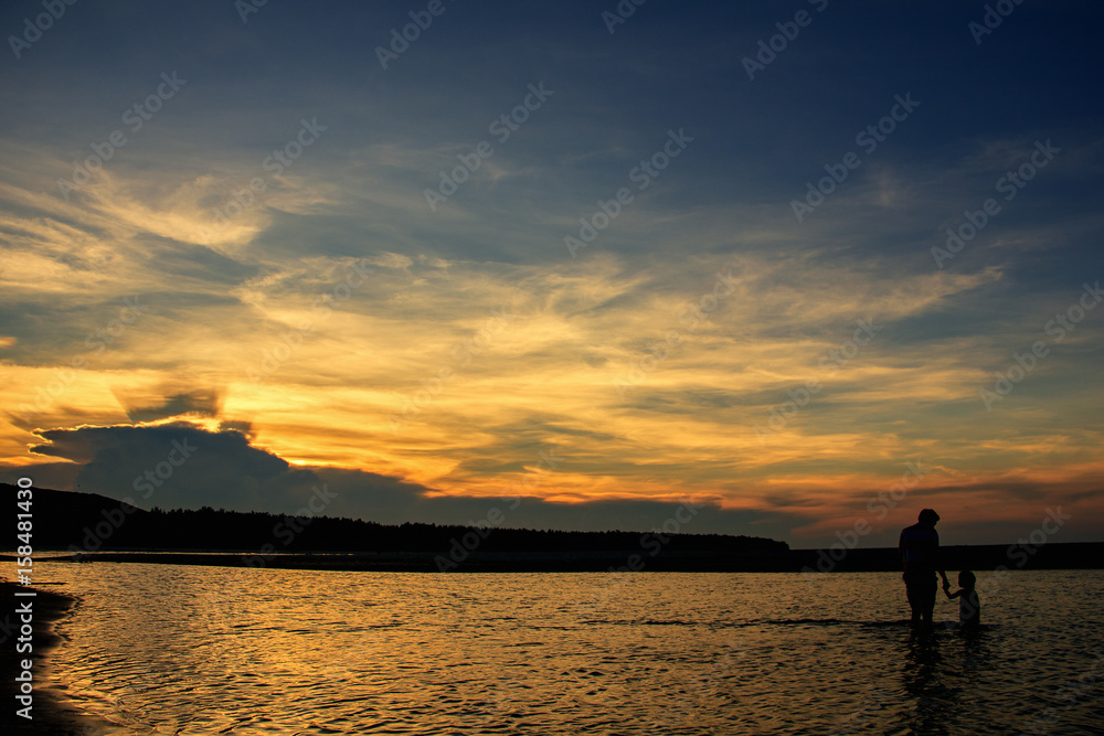 View of beach and sky during sunset which has father and his daughter in water (silhouette style)