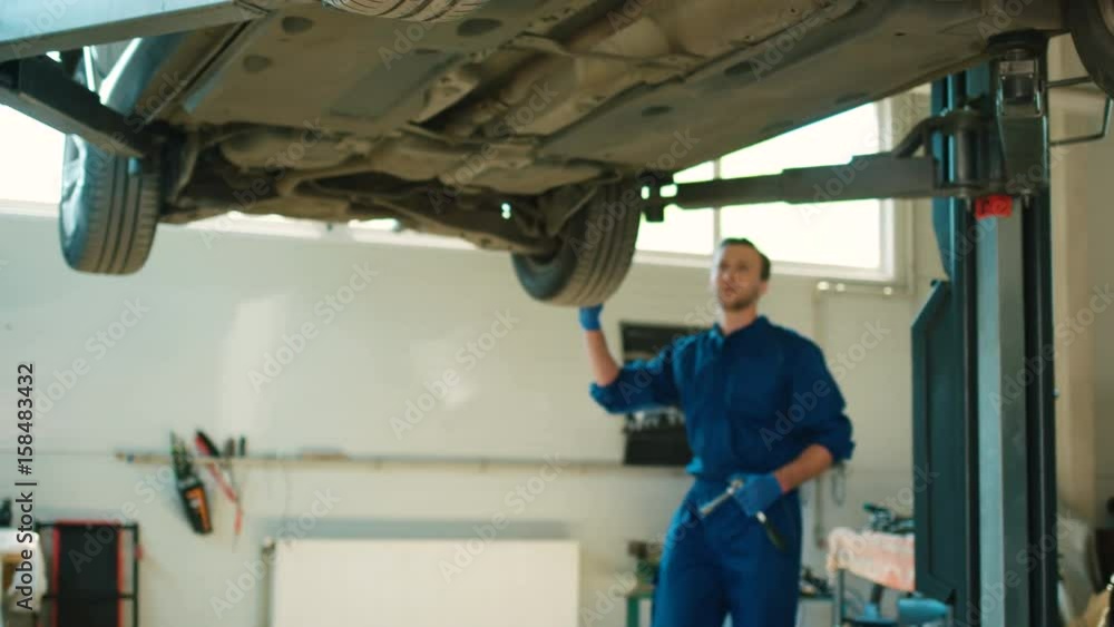 Caucasian handsome auto mechanic man in blue uniform using the cruciform key for examinating of car wheels fixing. Indoor. Caucasian handsome auto mechanic man in blue uniform using the cruciform key for examinating of car wheels fixing. Indoor.