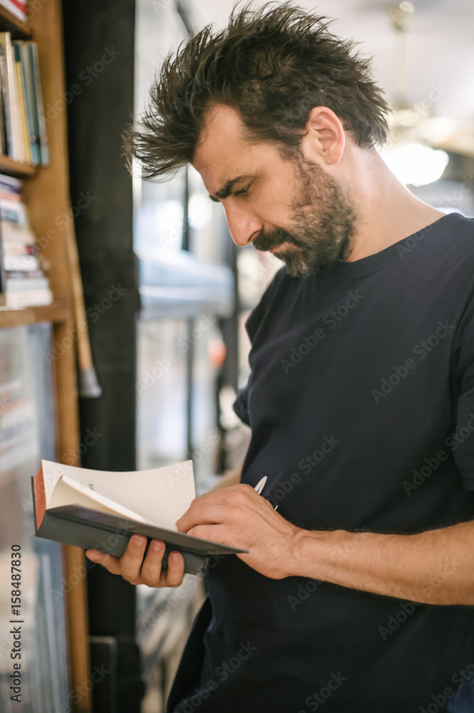 Curious man choosing book in his library at home Curious man choosing book in his library at home