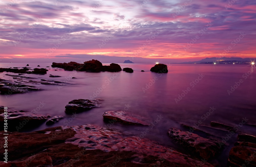 Obraz premium Dramatic dawning sky reflecting on peaceful sea water at the rocky beach of Yilan Coast Geologic Park in northeast Taiwan ~ Beautiful sunrise scenery of a rocky coast in rosy twilight (Long Exposure)