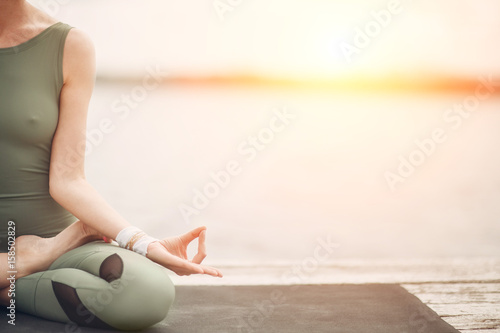 Yoga symbol. Lotus pose at the lake on sunset. Stylish modern woman. photo