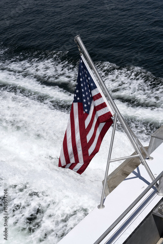 The American Stars and Stripes flag mounted on the stern of a bot with the wash as a backdrop,