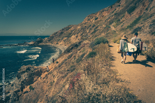 Young couple walking on a rugged trail with their surfboards in