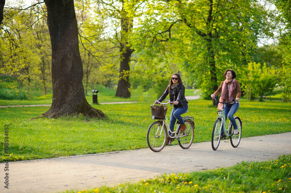 Fototapeta premium Two young women ride bikes in the spring park.