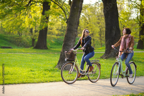 Two young women ride bikes in the spring park.