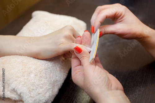 The master of the manicure saws and attaches a nail shape during the procedure of nail extensions with gel in the beauty salon. Professional care for hands. photo