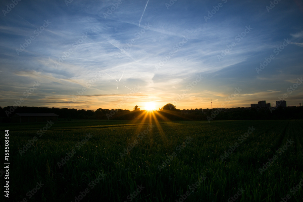 Sunset over green fields with a barn and television tower in background