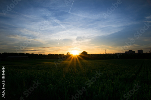 Sunset over green fields with a barn and television tower in background