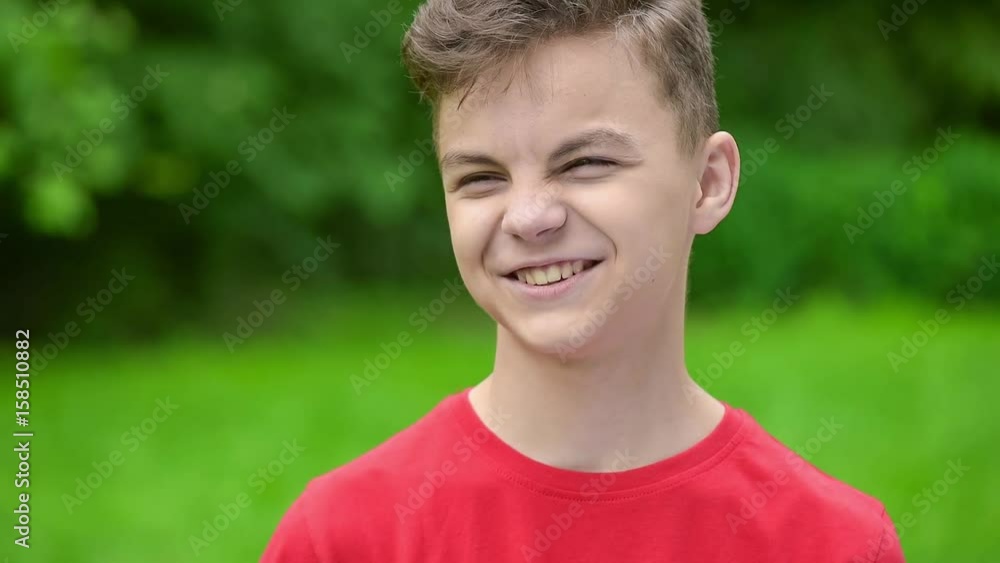 Happy caucasian teen boy - outdoor in nature portrait. Child in spring or summer city park. Slow motion close-up. Funny cute teenager smiling and looking at camera. Happy caucasian teen boy - outdoor in nature portrait. Child in spring or summer city park. Slow motion close-up. Funny cute teenager smiling and looking at camera.