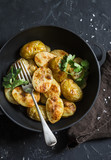 Baked new potatoes with coriander in a cast iron skillet on the dark table, top view. Vegetarian lunch or snack