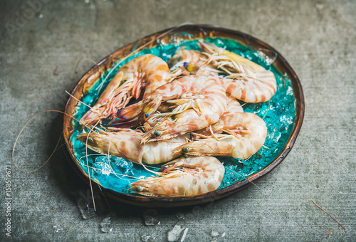 Raw uncooked tiger prawns on chipped ice in turquoise blue tray over grey concrete background. Fresh seafood