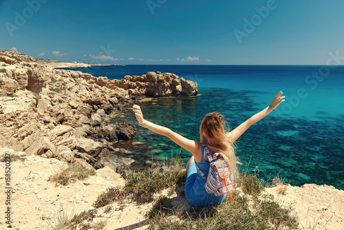 Beautiful young woman is looking to the sea being on the picturesque cliffy coast. She is holding her arms wide open.. Cape Greko. Cyprus.